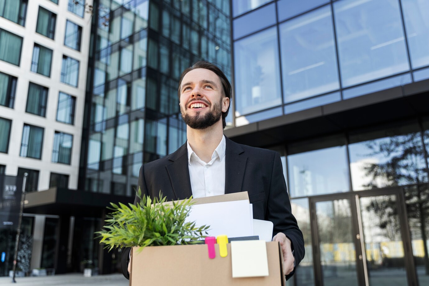 man smiling leaving office building with box of belongs